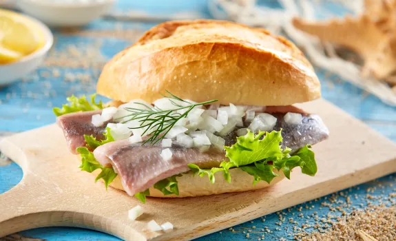 Delicious sandwich with fish and onion Yummy sandwich with pickled herring and chopped fresh onion served on wooden cutting board on blue table decorated in marine style
